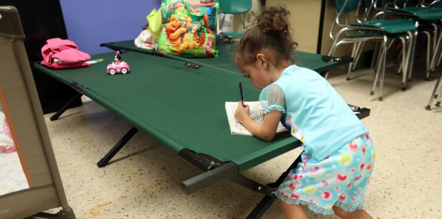 Una niña escribe en una libreta sobre uno de los catres que se colocan en los refugios. (GFR Media) (horizontal-x3)