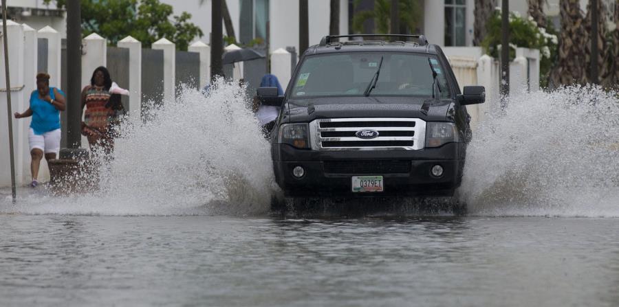 Una guagua pasa por un área inundada, mientras unas mujeres se mojan mientras caminan por la acera. (GFR Media) (horizontal-x3)