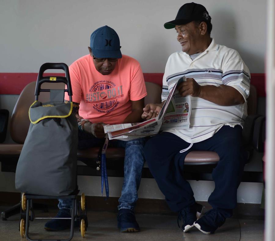 Los pacientes de diálisis Elías Salgado, de 56 años, y Edwin Alvarado, de 59, bromean mientras leen el periódico en el aeropuerto de Vieques, donde esperaban para embarcar en un avión que los trasladaría para recibir tratamiento. (semisquare-x3)
