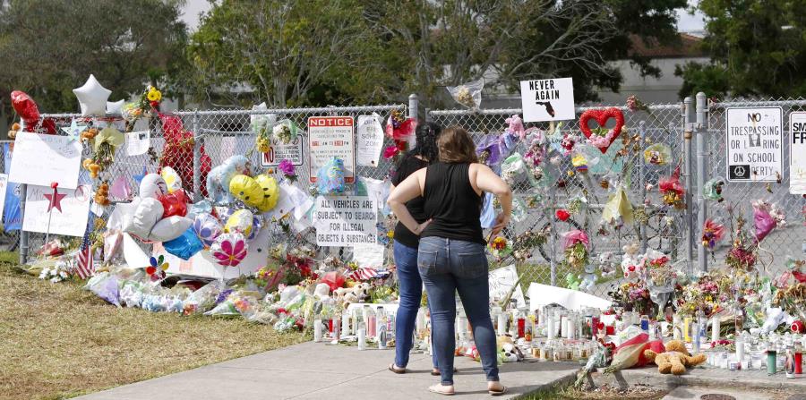 Dos personas observan un altar improvisado en memoria de las víctimas del tiroteo en la Escuela Secundaria Marjory Stoneman Douglas en Parkland, Florida. (horizontal-x3)