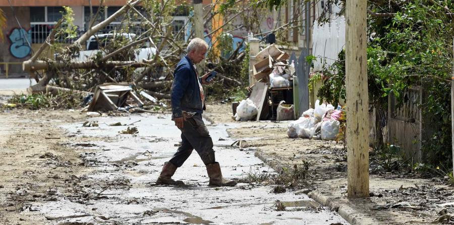 Un hombre cruza una calle llena de fango y escombros en el barrio Buenos Aires en Arecibo. (horizontal-x3)