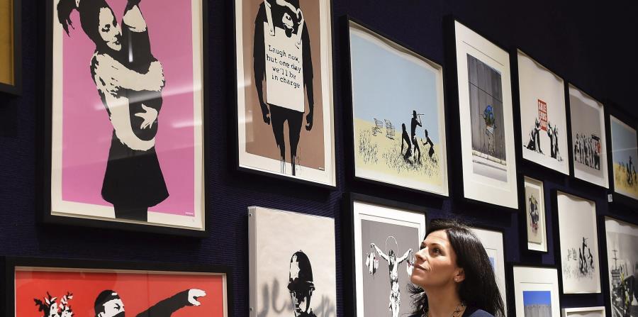 Una empleada de la casa de subastas Bonhams contempla las obras del grafitero británico Bansky, expuestas para los medios en Londres. (EFE) (horizontal-x3)
