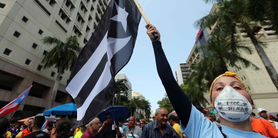 Una mujer levanta una bandera de Puerto Rico con los colores blanco y negro durante una protesta contra la Junta de Supervisión Fiscal. (GFR Media) (horizontal-x3)