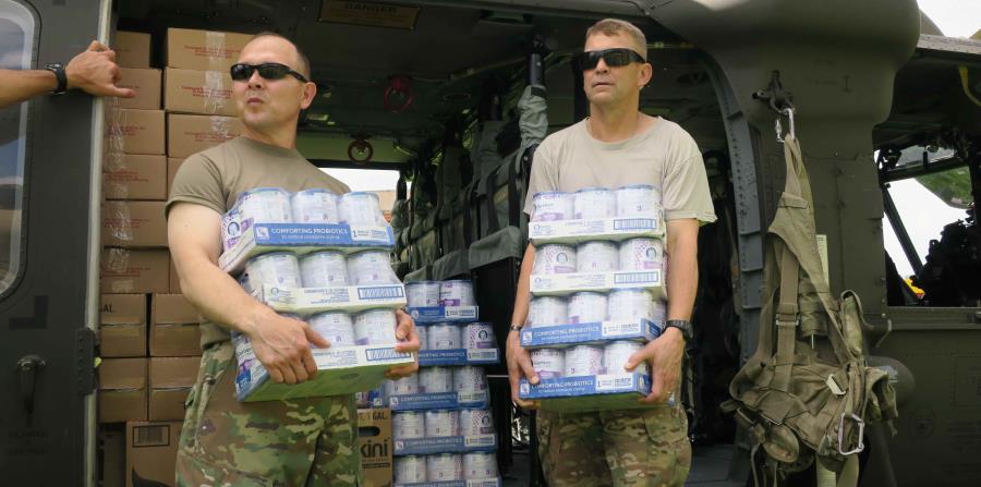 El general Jeffrey Buchanan (derecha) junto a otro militar cargan cajas de comida para bebés en una visita a Jayuya. (horizontal-x3)
