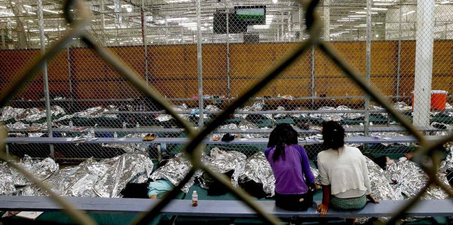 dos jóvenes ven un partido del Mundial de fútbol en un televisor desde la zona en la que están recluidas con cientos de niños migrantes centroamericanos en un centro de la patrulla fronteriza de Estados Unidos en Nogales, Arizona. (AP (horizontal-x3)