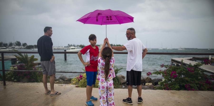 Una niña aguanta una sombrilla mientras observa el mar junto a otras personas. (GFR Media) (horizontal-x3)