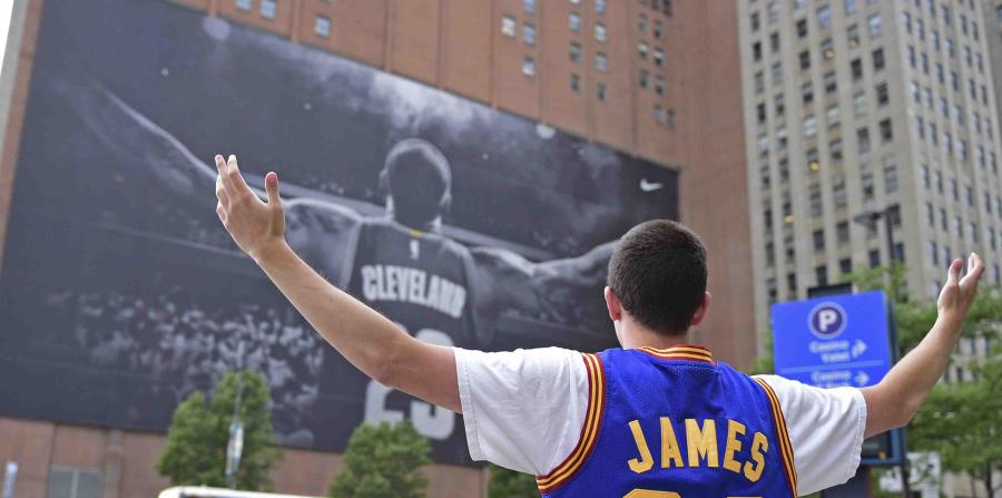 Un fanático de LeBron James se toma una foto junto al gigante afiche del astro de la NBA en Cleveland. (AP) (horizontal-x3)