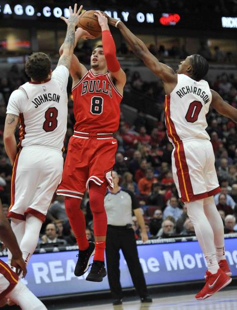 Zach LaVine, de los Bulls de Chicago, salta para disparar entre Tyler Johnson y Josh Richardson, del Heat de Miami, en la segunda mitad del partido. (vertical-x1)