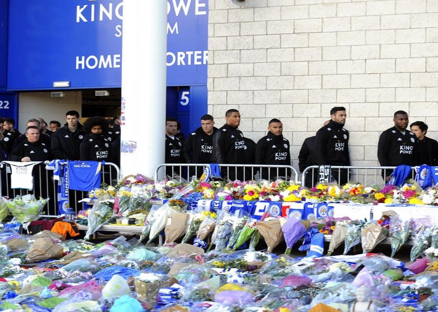 Los jugadores del Leicester City observan los tributos que deja la gente frente al estadio tras el acciedente de un helicóptero en el que murieron el propietario del club Vichai Srivaddhanaprabha y otras cuatro personas. (semisquare-x3)