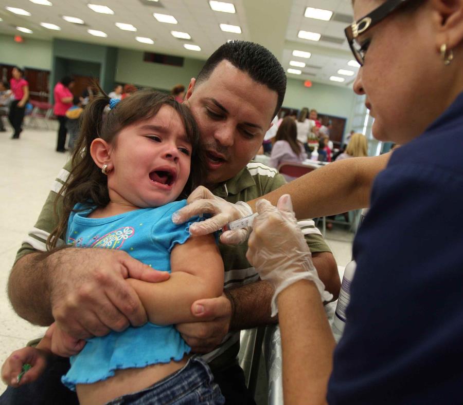 Un padre sujeta a su hija mientras una profesional de la salud la vacuna. (GFR Media) (semisquare-x3)