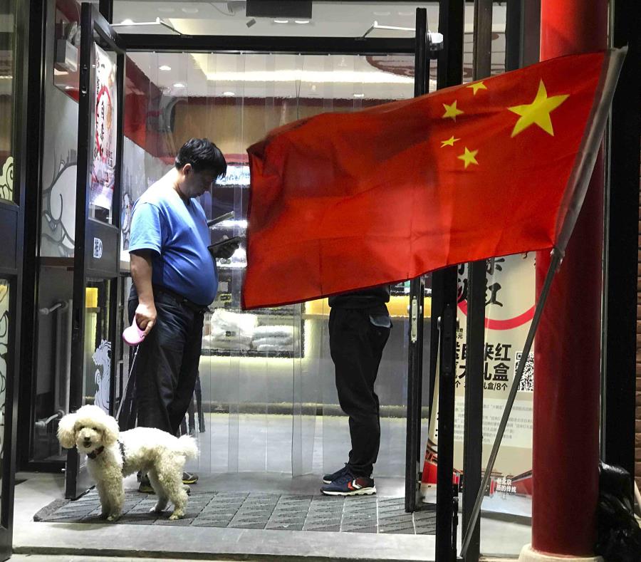 En esta imagen de archivo, tomada el 3 de octubre de 2017, un hombre pase a su parro a la salida de un restaurante ante el que ondea una bandera china, en Beijing, China (semisquare-x3)