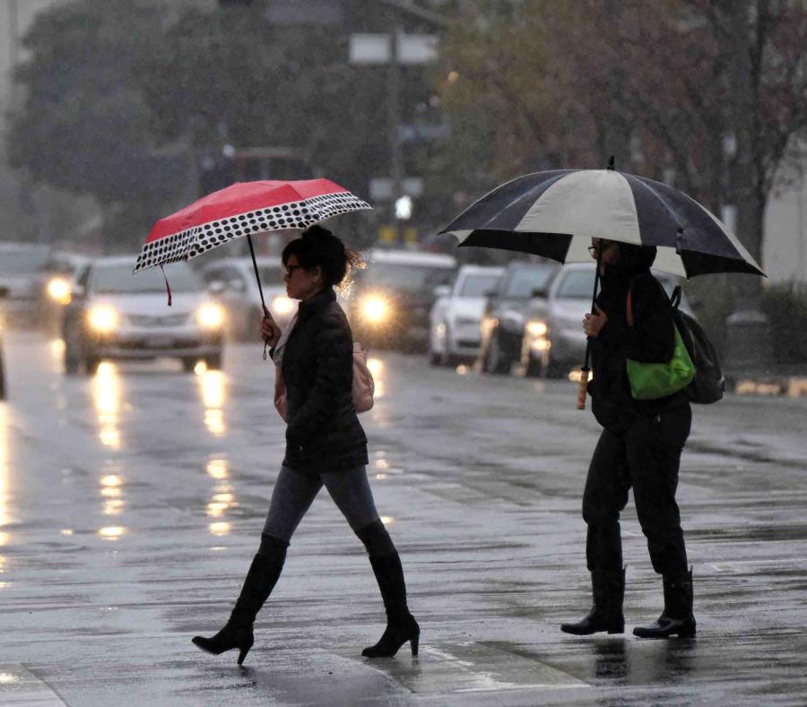 Dos mujeres se cubren con sombrillas de la lluvia, mientras caminan por una carretera. (semisquare-x3)