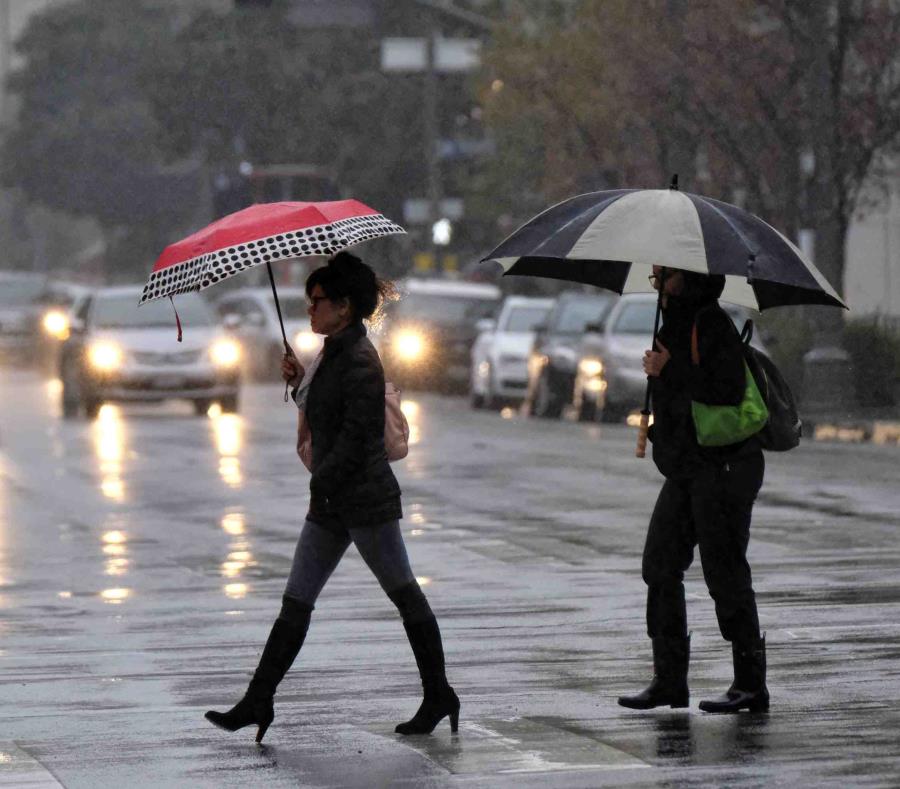 Dos mujeres se cubren con sombrillas de la lluvia, mientras caminan por una carretera. (Archivo / AP) (semisquare-x3)
