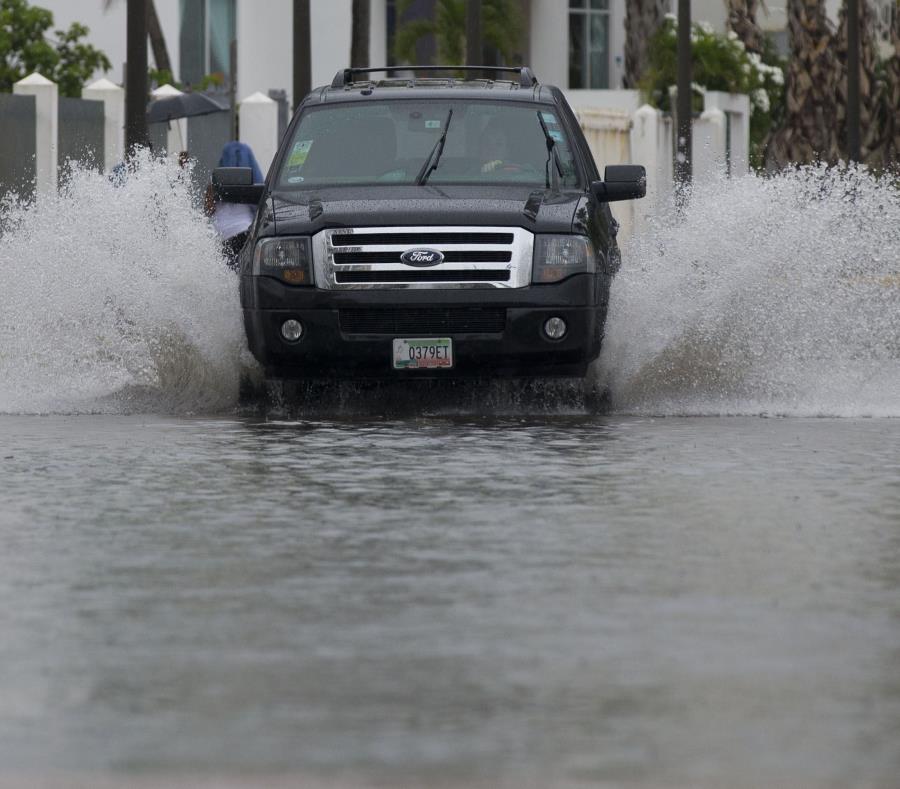 Una guagua pasa por un área inundada, mientras unas mujeres se mojan mientras caminan por la acera. (GFR Media) (semisquare-x3)