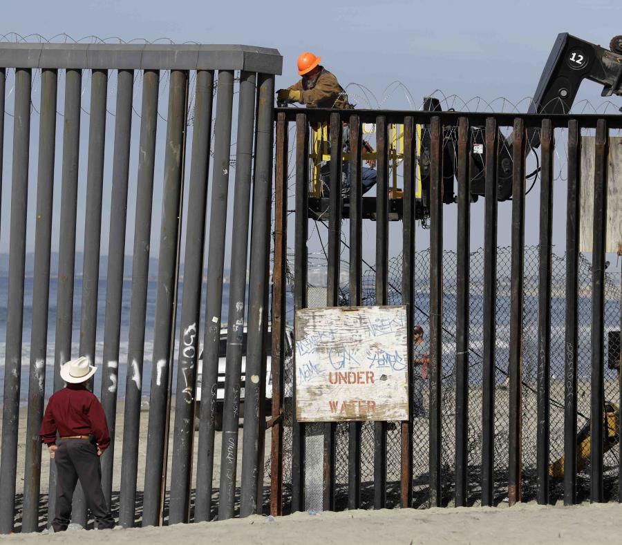 Un hombre en el lado estadounidense de la frontera (arriba) trabaja en la estructura ante la mirada de otro desde la playa, en Tijuana, México. (semisquare-x3)